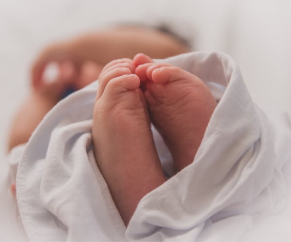 Close-up of a babys feet and toes wrapped in a white blanket, symbolizing the tender journey of infant adoption. The softly blurred background highlights the small size and intricate detail of these precious feet.